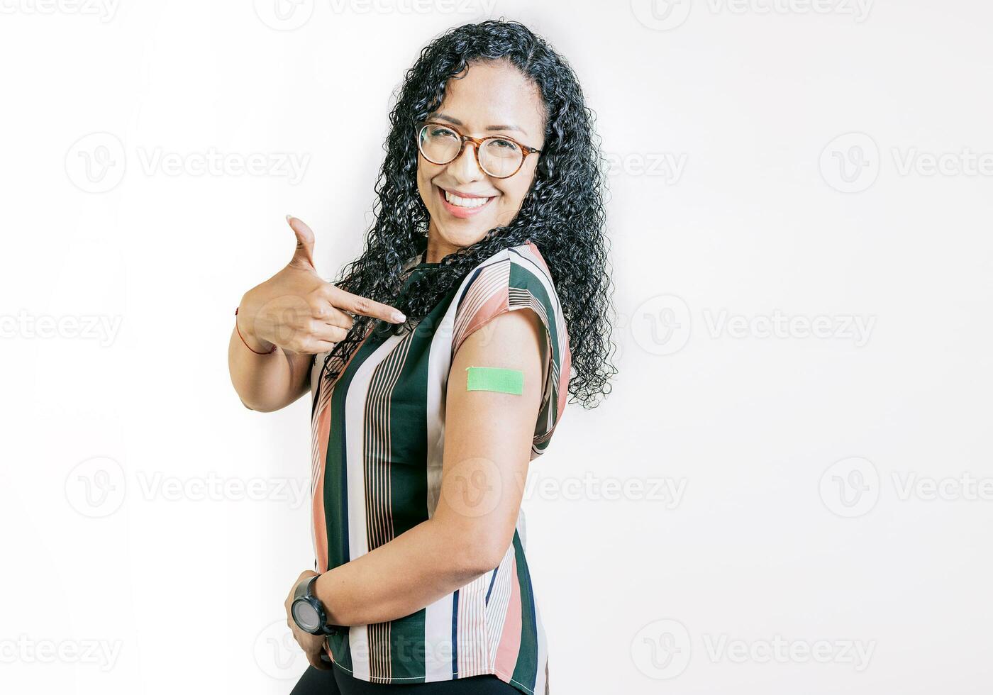 Smiling woman pointing at her vaccinated arm. Latin woman pointing at the bandage on her vaccinated arm photo