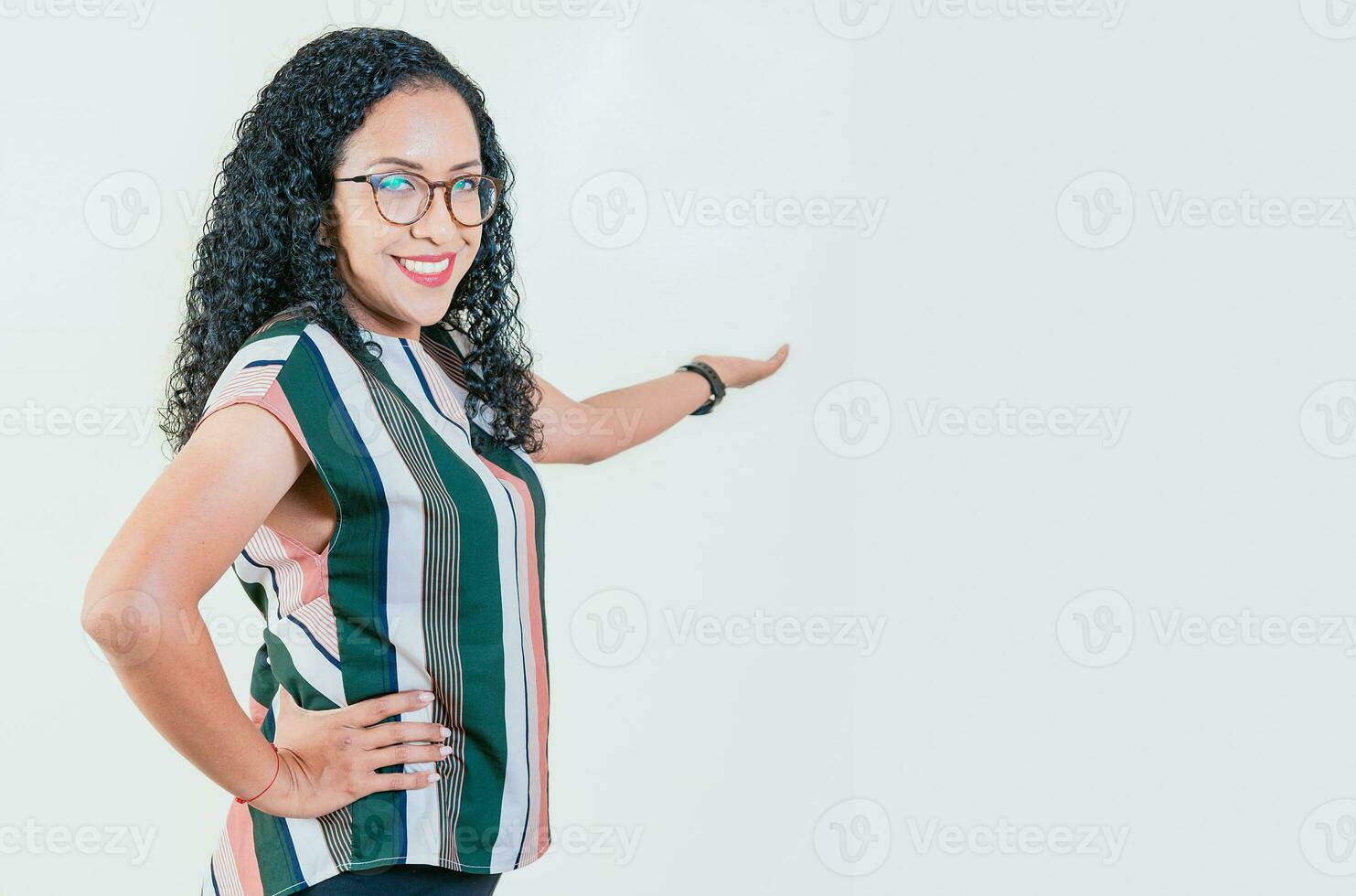 Smiling young afro woman welcoming you isolated. Happy afro girl pointing back presenting a product isolated. Cheerful people pointing a promotion with her palm photo