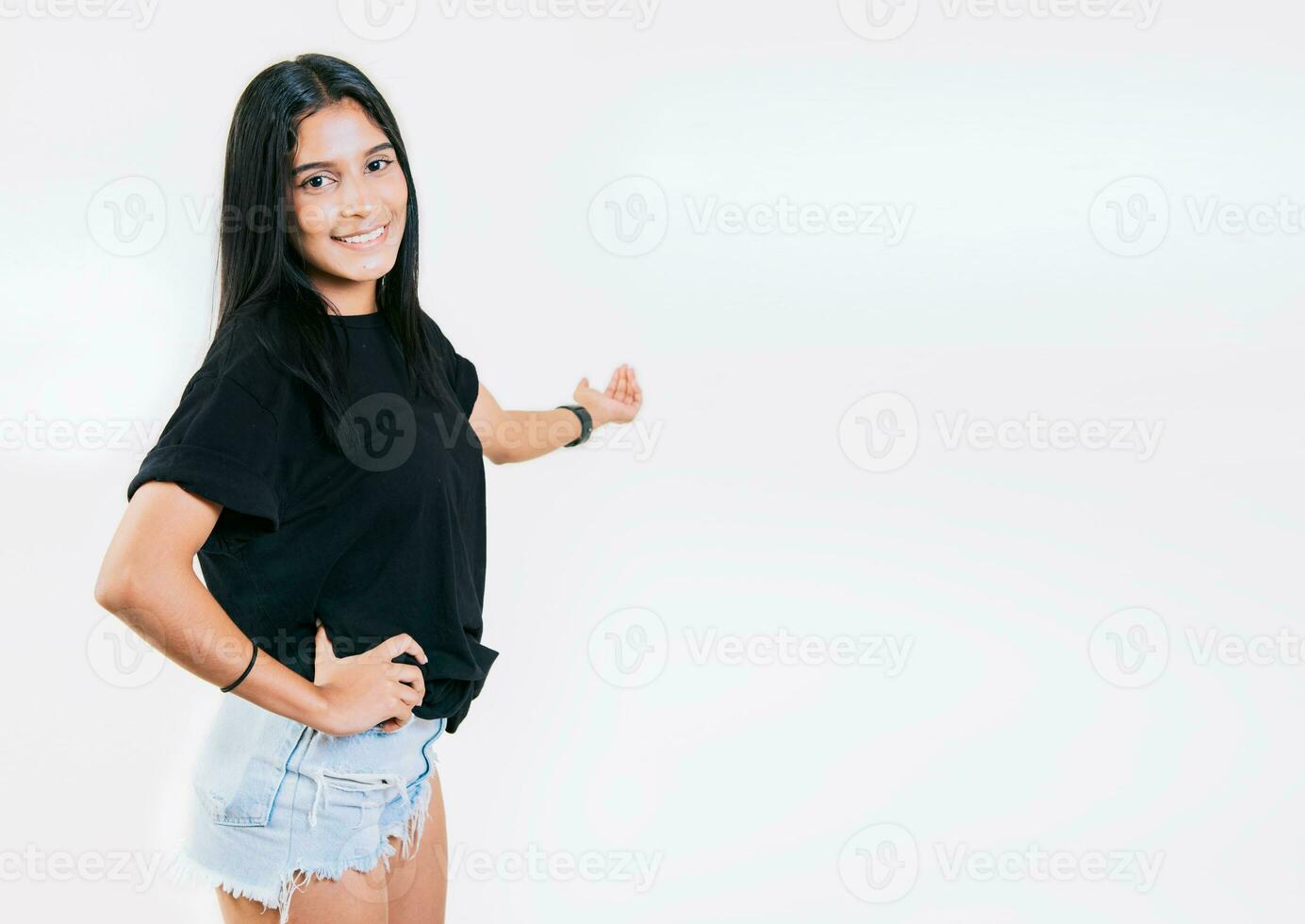 Happy young girl welcoming you isolated. Smiling latin girl pointing back presenting a product. Latin girl pointing a promotion with her palm photo