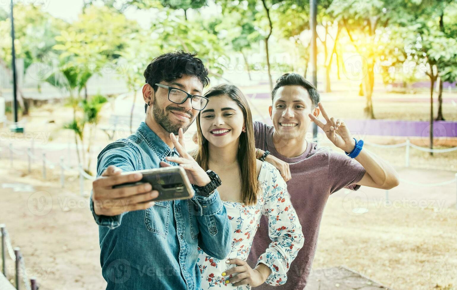 Happy friends taking a selfie in a park. Three friends standing taking a selfie in the park. Portrait of three smiling friends taking a selfie on the street. Friendship and selfie concept photo