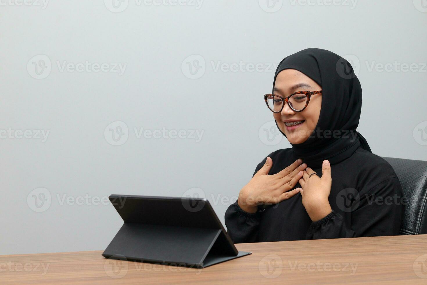 Portrait of attractive Asian hijab woman working on her tablet. Muslim girl doing task in office. Employee and freelance worker concept. photo