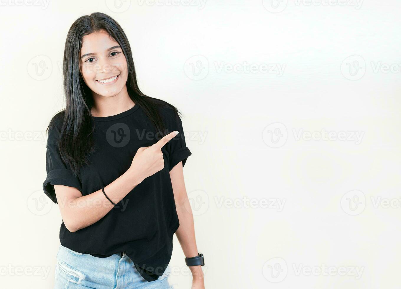 Smiling teenage girl pointing side with hand. Cheerful latin girl pointing an offer isolated. Happy teenager pointing a promo isolated photo