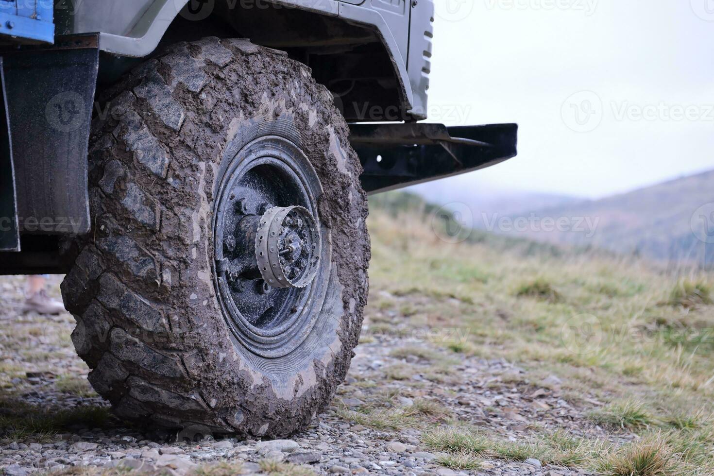 Wheel closeup in a countryside landscape with a mud road. Off-road 4x4 suv automobile with ditry body after drive in muddy road photo
