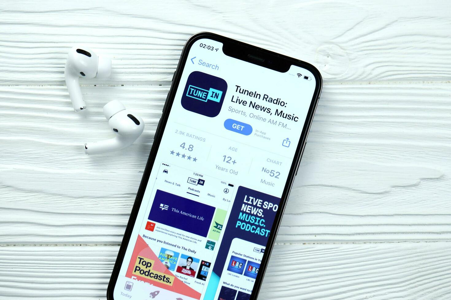 KHARKOV, UKRAINE - MARCH 5, 2021 TuneIn music icon and application from App store on iPhone 12 pro display screen with airpods pro on white table photo
