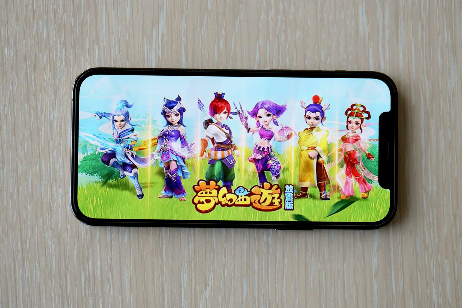 Fantasy Westward Journey mobile iOS game on iPhone 15 smartphone screen on wooden table during mobile gameplay photo