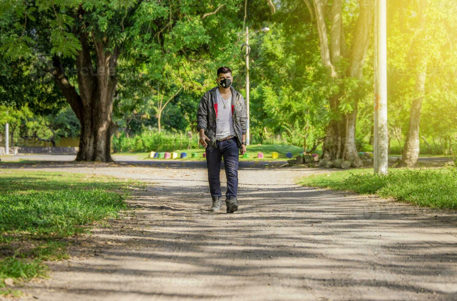 Man walking in the street with face mask on, man walking head-on in the street with face mask, young man with mask walking down the street photo