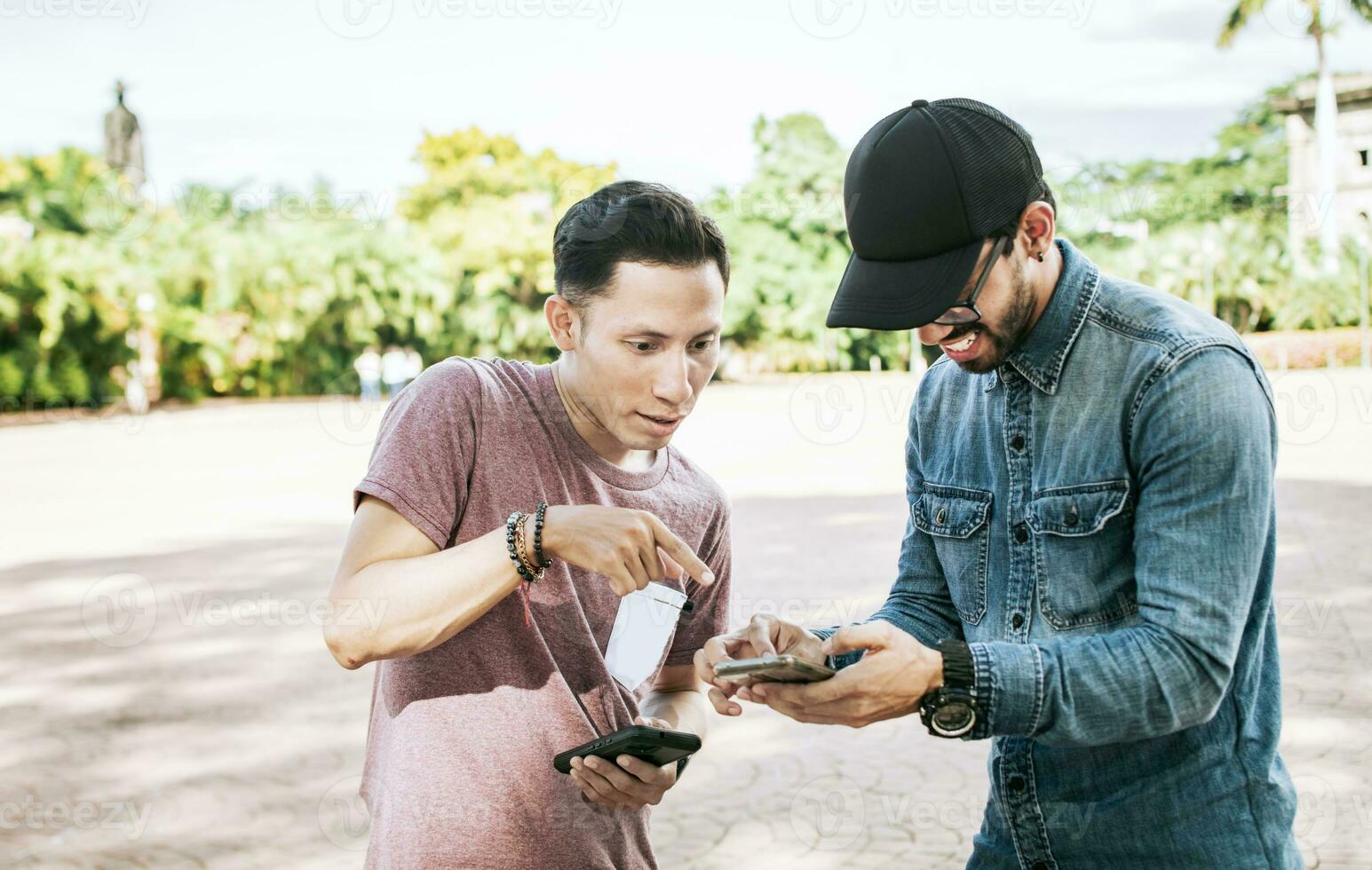 dos Adolescente chicos comprobación su célula Los telefonos en el calle, dos chicos comprobación un célula teléfono al aire libre, dos joven hombres mirando medios de comunicación en un célula teléfono en el calle foto