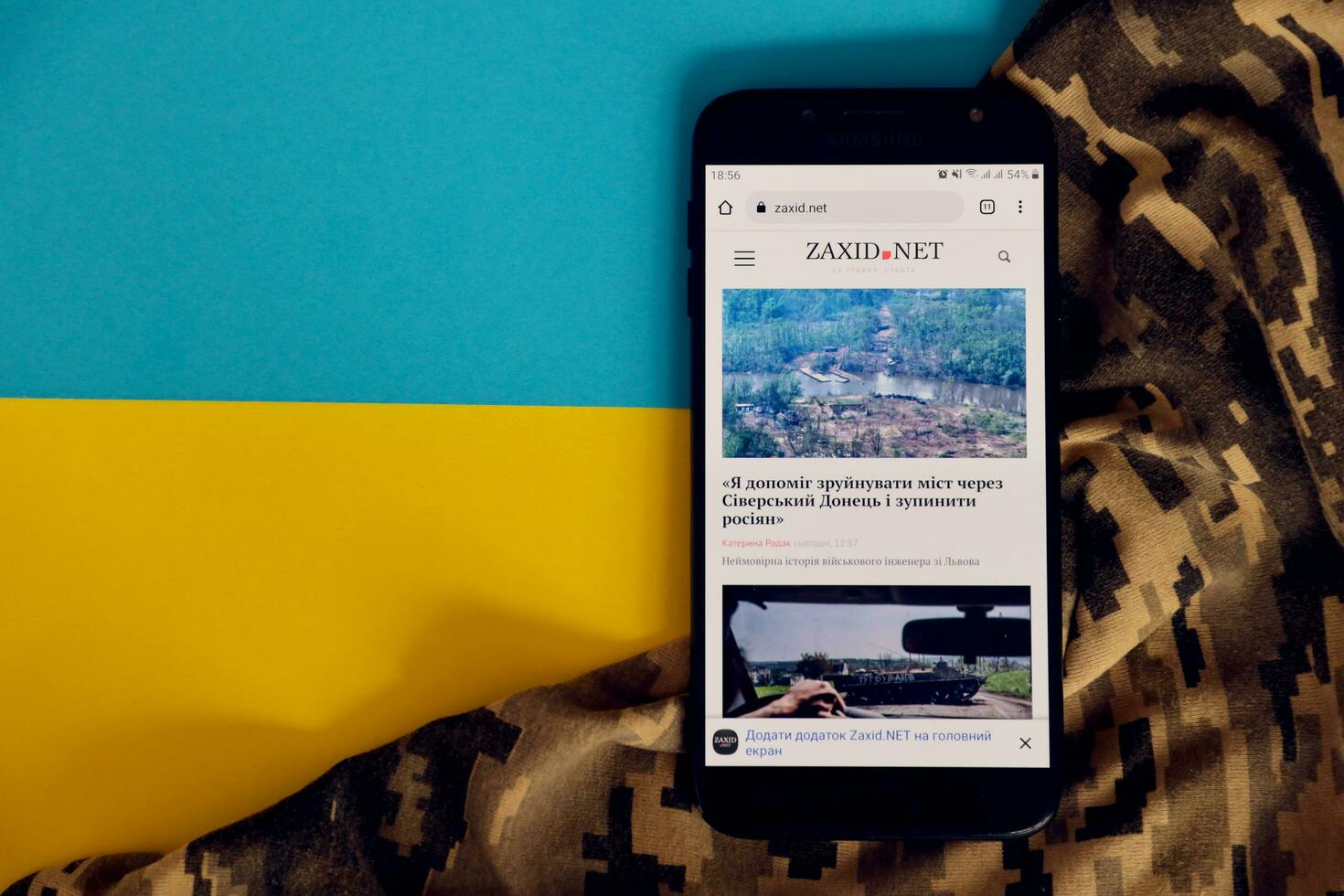 KYIV, UKRAINE - 4 MAY, 2023 Zaxid Net ukrainian news portal on smartphone screen with ukrainian flag and camouflage fabric photo