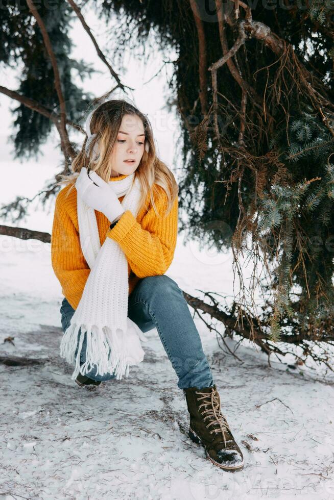 adolescente rubia en un amarillo suéter fuera de en invierno. un Adolescente niña en un caminar en invierno ropa en un Nevado bosque foto