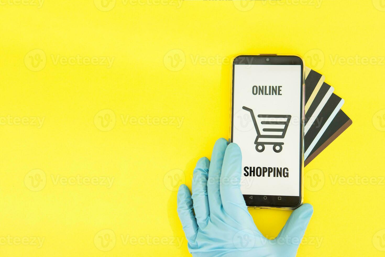 Close-up of hands in medical gloves with a smartphone. Online shopping, online banking, online payment. Payment with plastic cards. Flat Lay on a yellow background. photo