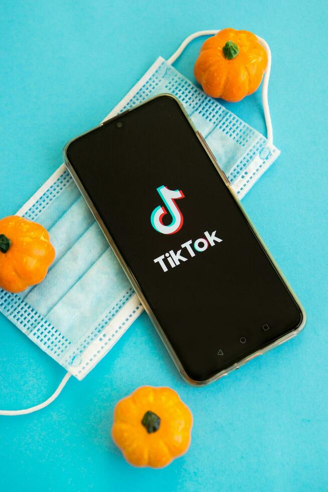 Tver, Russia, September 25, 2020, medical mask, pumpkins and tik Tok logo on the smartphone screen on blue background. Tik-Tok icon. the tik Tok app. Tiktok social network. photo