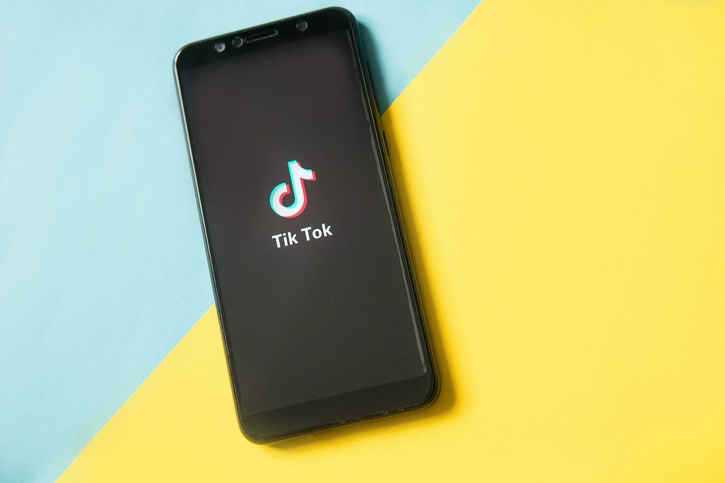 Tver, Russia - February 28, 2020 Tik tok logo on smartphone screen on blue and yellow background. Tik Tok icon. tik tok application. Tiktok Social media network. Space for text. photo
