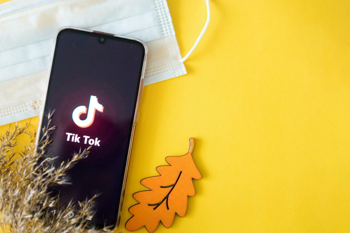 Tver, Russia-April 9, 2020, The tik tok logo on a smartphone screen on an yellow background with a medical mask and dry grass. Tik-Tok icon. the tick Tok app. Tiktok social network. photo