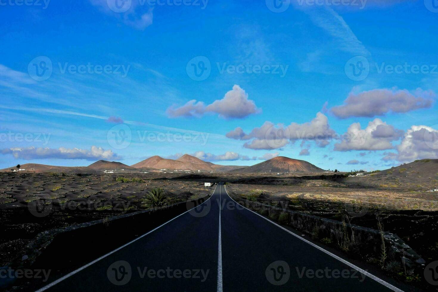 an empty road in the middle of a desert with mountains in the background photo