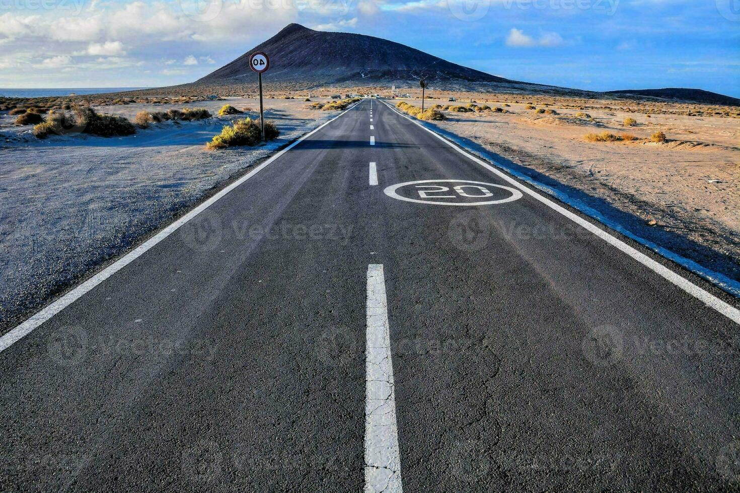 an empty road in the middle of a desert with a mountain in the background photo