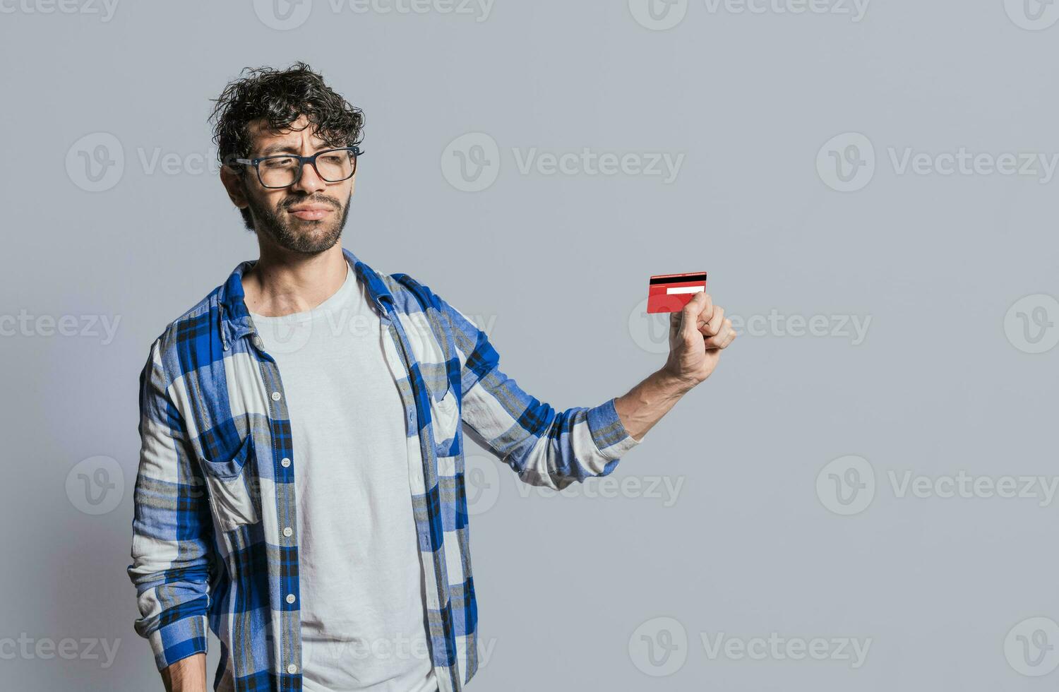 Person holding and looking at credit card with distrust, Confused handsome man holding credit card isolated. Insecure young man holding a credit card. Concept distrust with credit cards photo