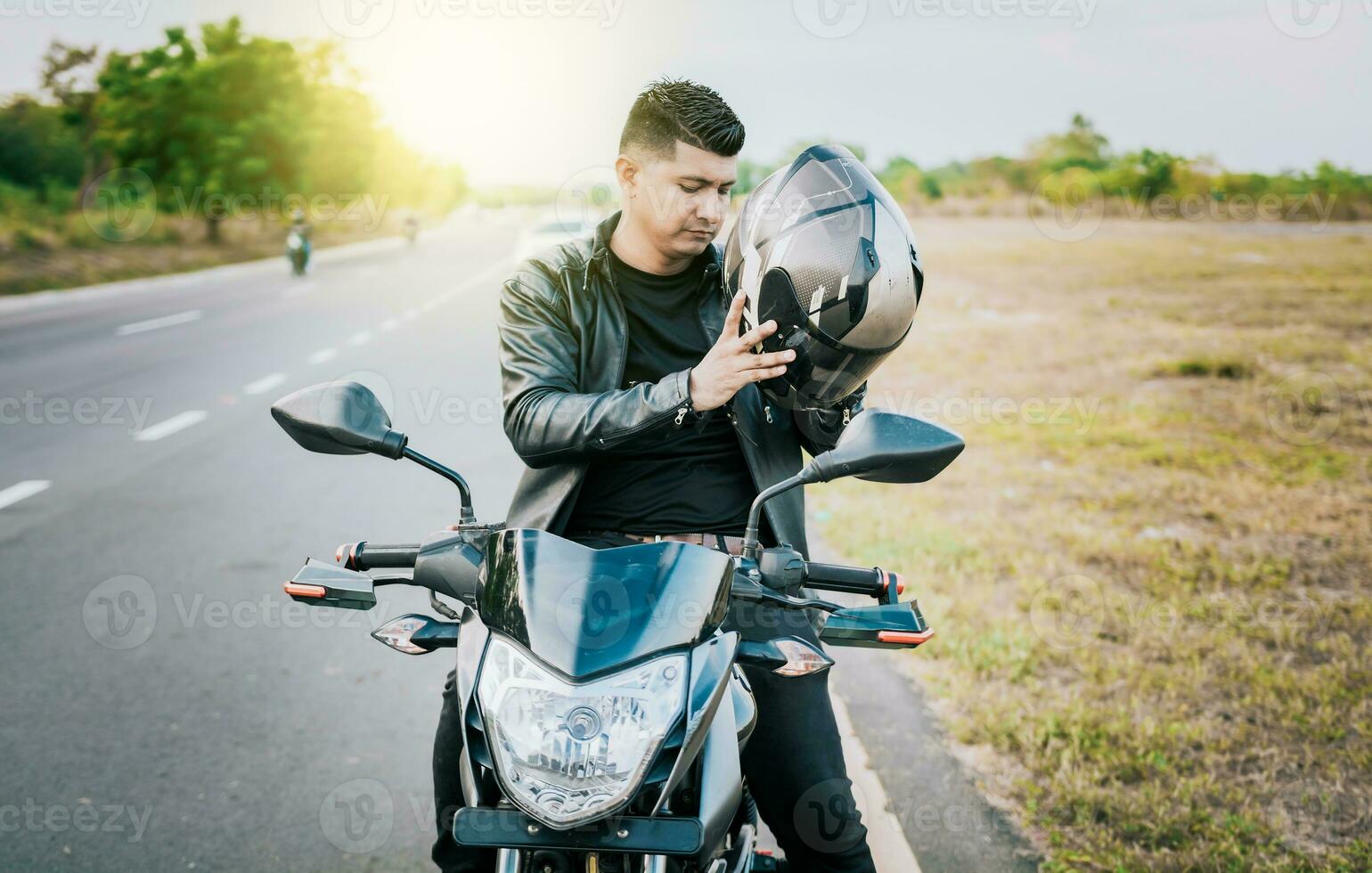 Young motorcyclist man putting on safety helmet outdoors. Male biker on motorcycle putting on helmet. Biker motorcycle safety concept photo