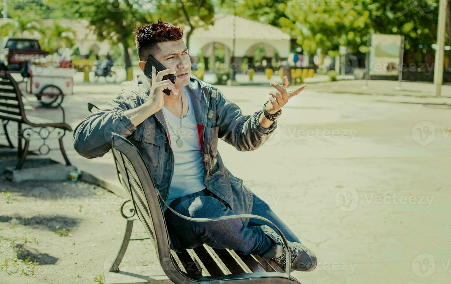 Man sitting on a bench calling on the phone, young man sitting on a bench with cell phone, close up of a young man calling on the phone sitting on a bench photo