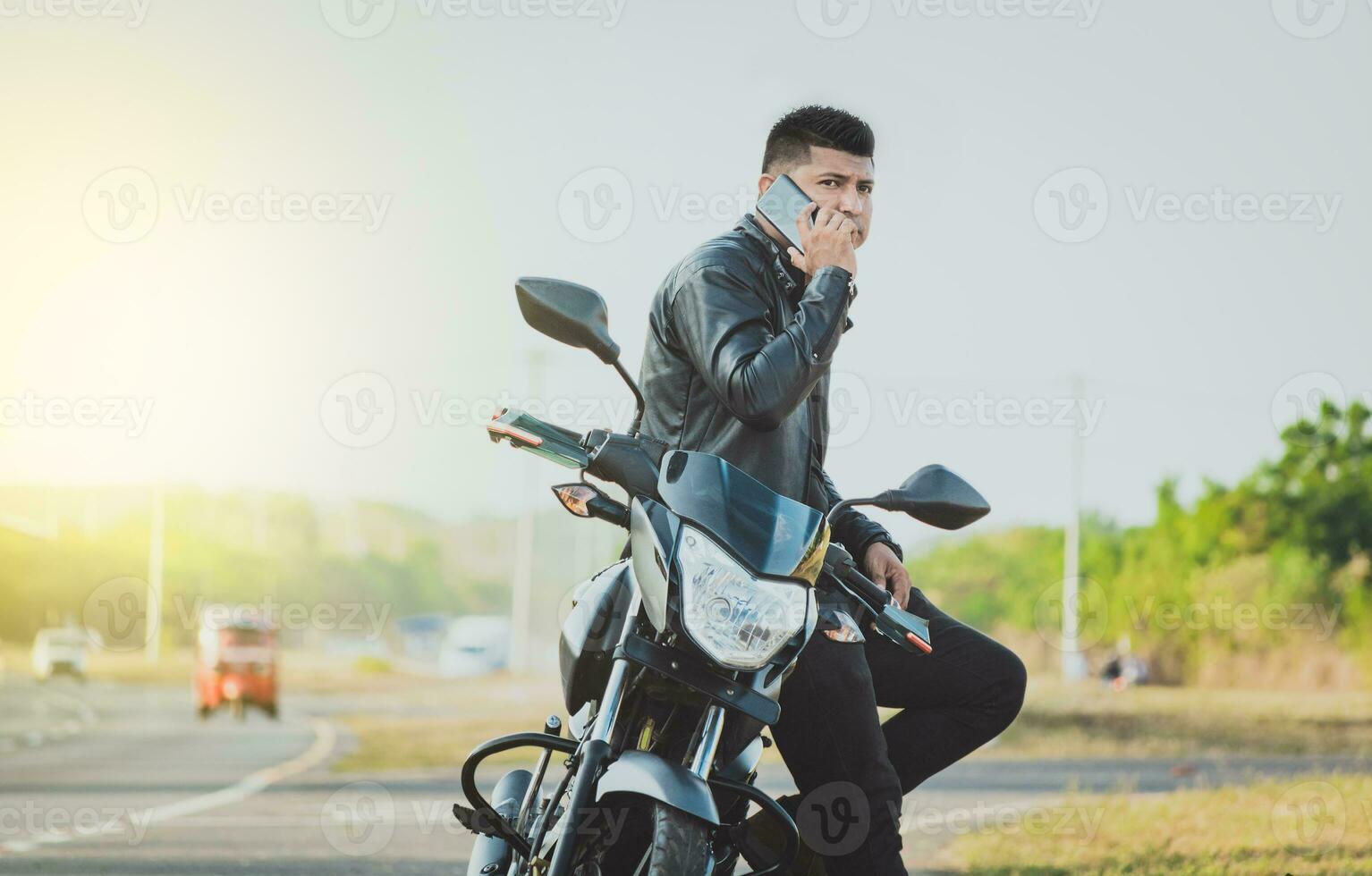 Biker sitting on motorcycle calling on the phone on the roadside. Handsome biker calling on the phone in the street. Concept of motorcyclist using the phone photo