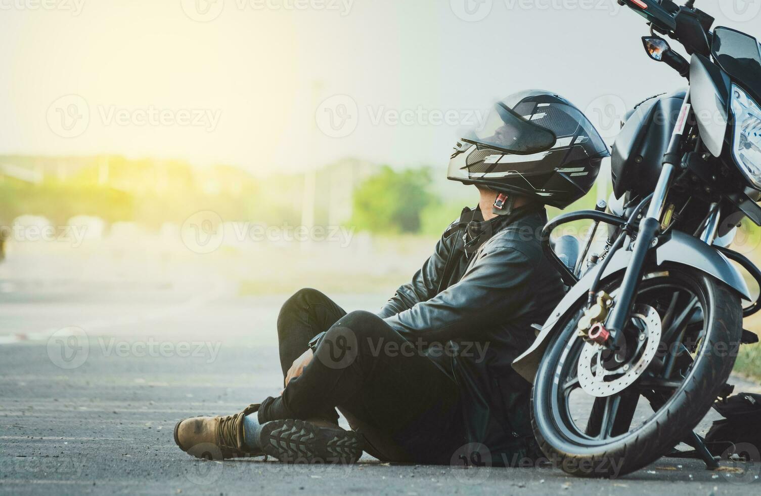 motorista sentado siguiente a su motocicleta en el la carretera. masculino motociclista sentado y propensión en su motocicleta en el asfalto foto