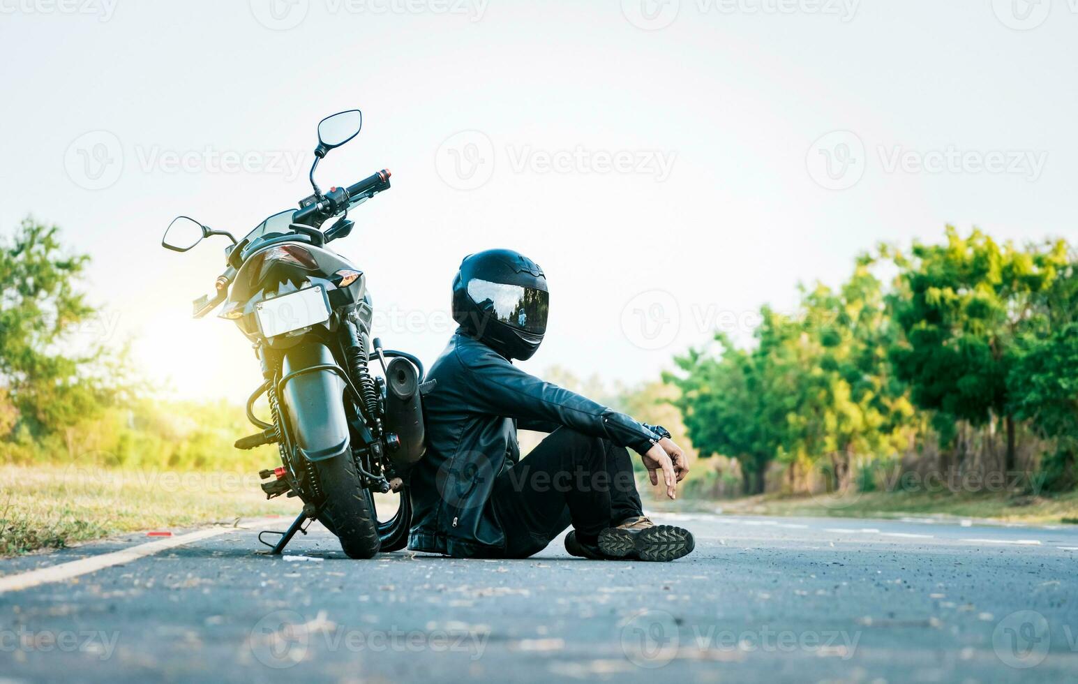 masculino motorista sentado siguiente a su motocicleta en el la carretera. masculino motociclista sentado y propensión en su motocicleta en el asfalto foto