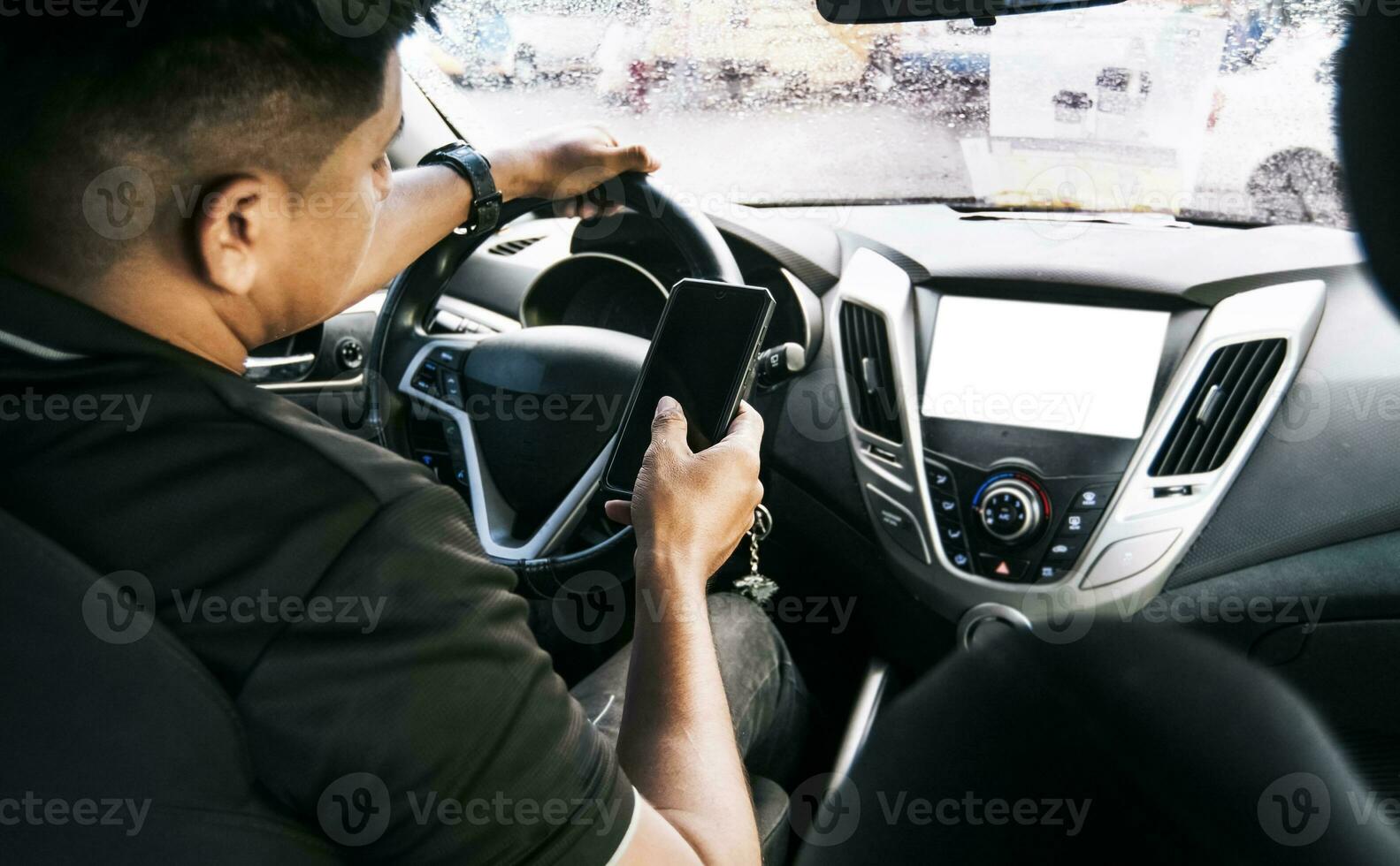 Person holding the cell phone and with the other hand the steering wheel, Distracted driver using the cell phone while driving, Man using his phone while driving, Concept of irresponsible driving photo