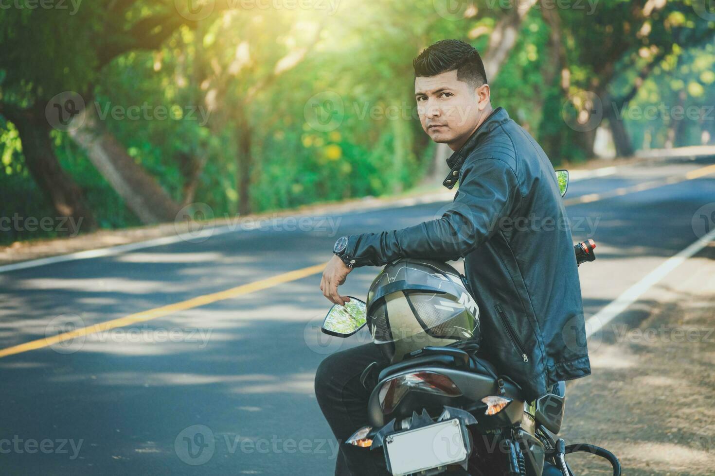 latín motociclista sentado en su moto cerca un asfalto la carretera. retrato de motorista en chaqueta sentado en su motocicleta a el lado de el la carretera foto