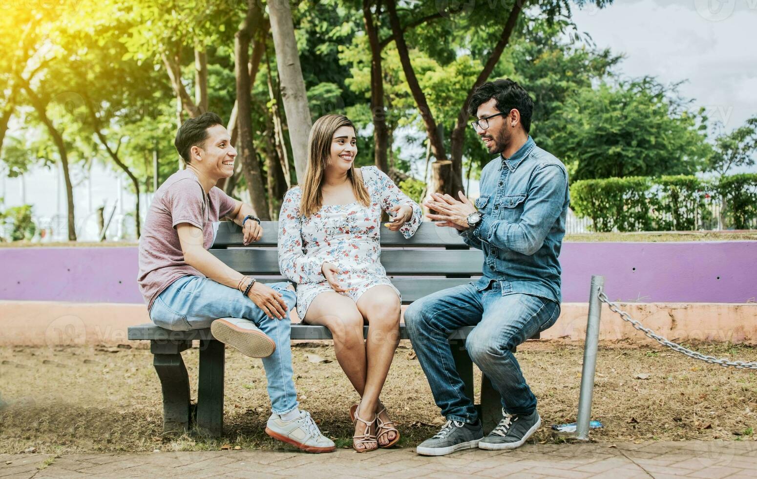 Tres contento amigos hablando en un parque. Tres Adolescente amigos hablando sentado en un parque banco, grupo de Tres amigos hablando sentado en un parque. concepto de personas hablando en el parque foto