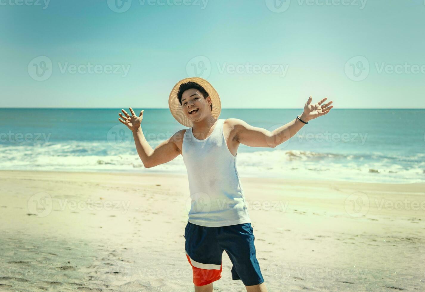 Portrait of man in hat on the beach spreading his arms. Smiling young man on the beach spreading arms looking at camera, Concept of man enjoying the beach photo