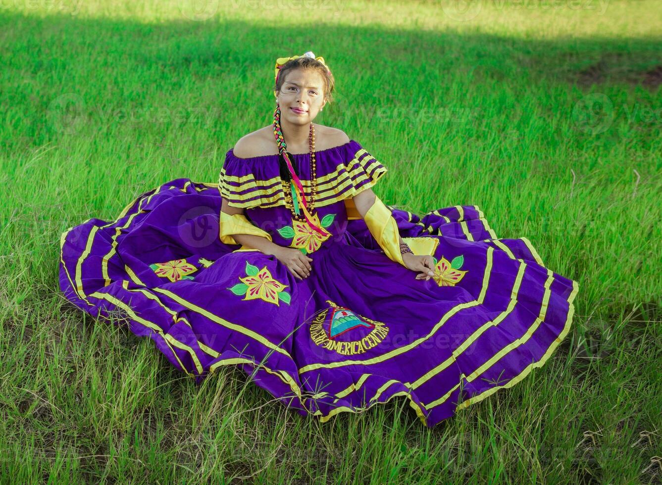 joven nicaragüense mujer en tradicional gente disfraz sentado en el césped en el campo, retrato de nicaragüense mujer en gente disfraz sentado en el césped foto