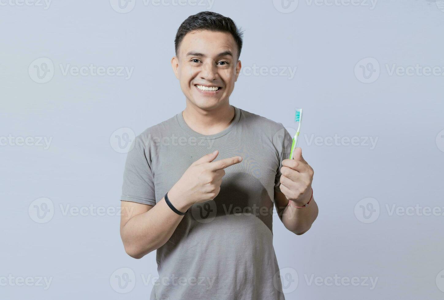 Handsome guy holding and pointing at toothbrush isolated. Person holding and pointing a toothbrush on isolated background, Smiling man holding and pointing at toothbrush photo
