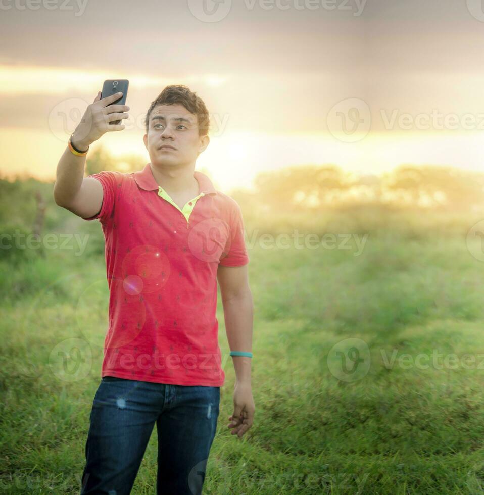Young man taking a picture, young man taking selfie in the field, young man in the field taking a picture photo