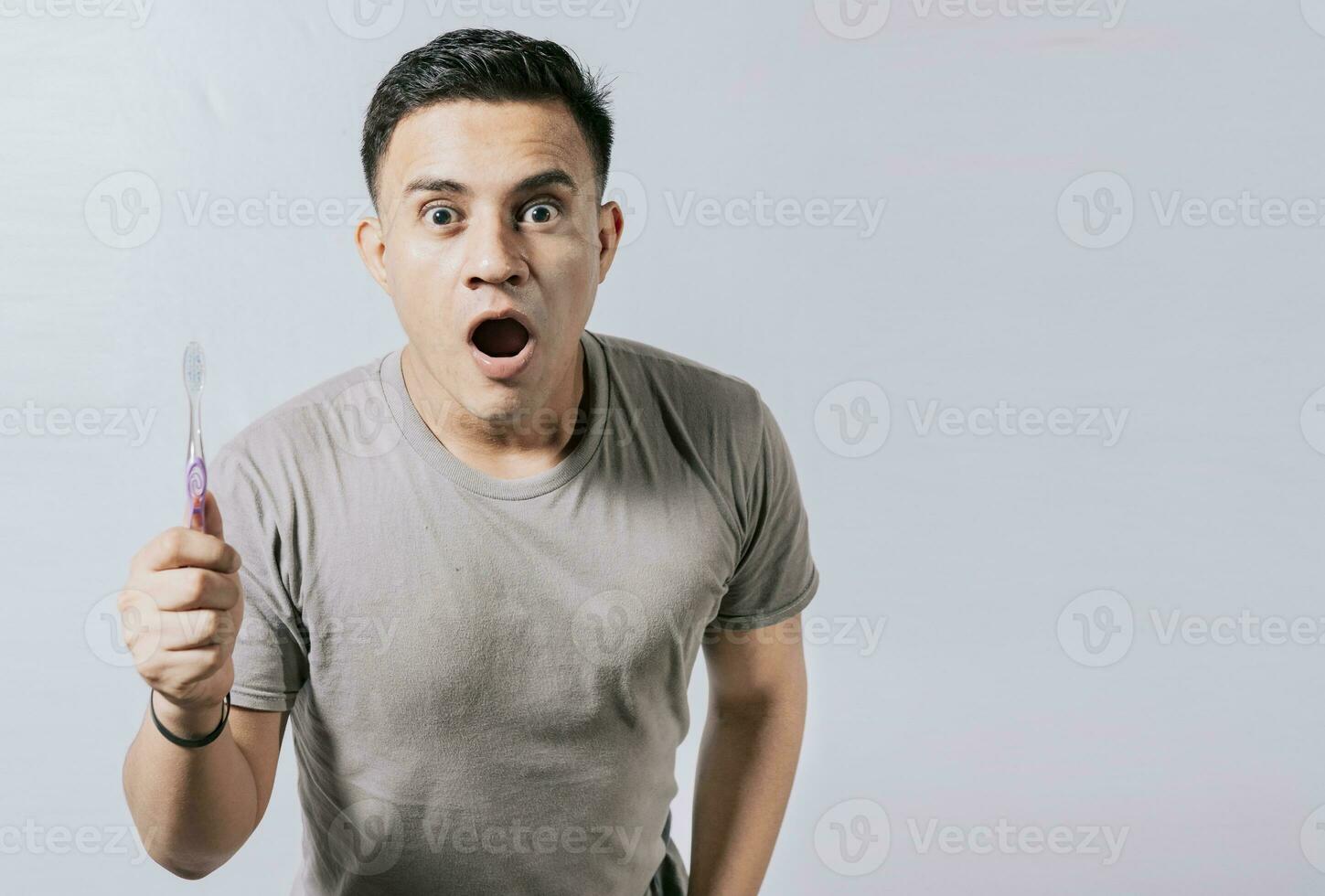 Guy holding toothbrush with amazed face isolated on white, Surprised young man holding a toothbrush. Amazed teenager holding toothbrush isolated photo