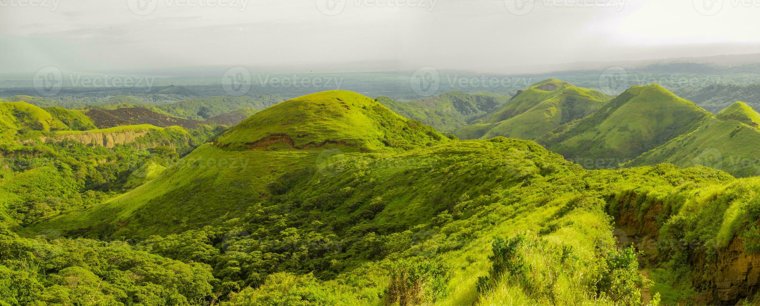 Image of a hill surrounded by other green hills, A path to a green hill with blue sky with copy space photo