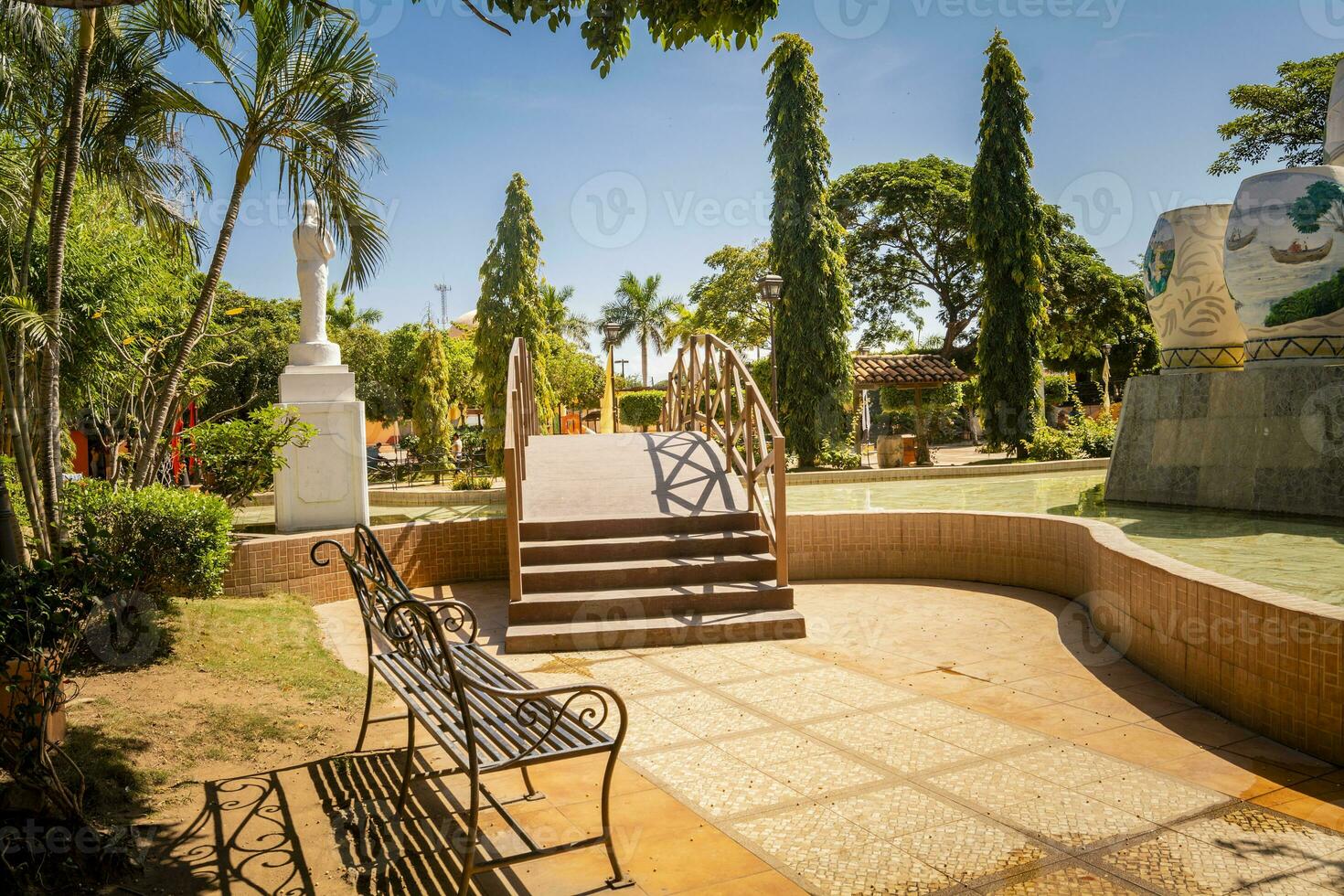 A nice and relaxed park with a wooden bridge over a water fountain, Traditional park of Nagarote, Nicaragua. View of a calm park with a small wooden bridge on a sunny day. Nagarote central park photo