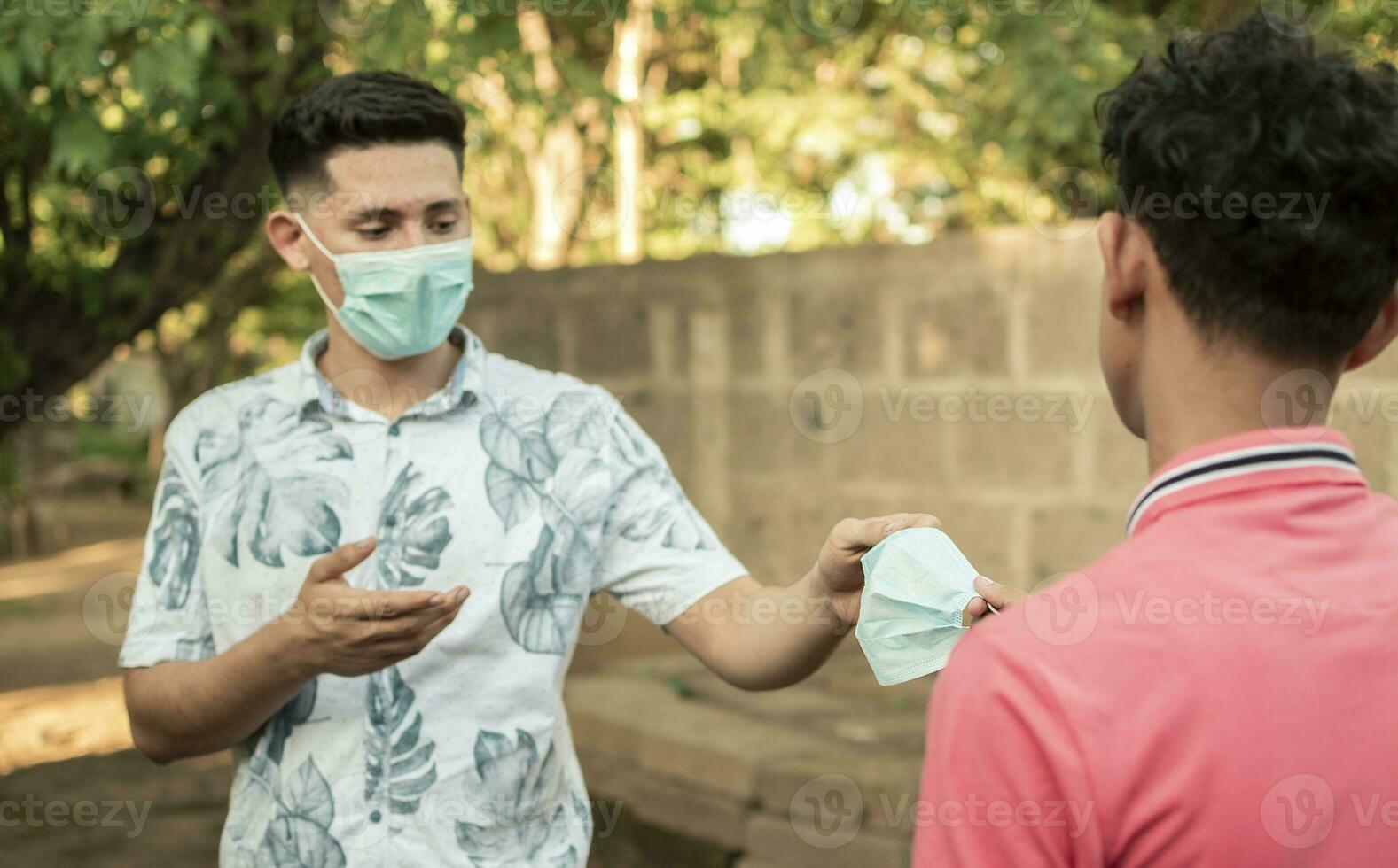 joven hombre compartiendo máscara a otro joven hombre, joven hombre dando un máscara a otro joven hombre, concepto de dando un mascarilla, foto