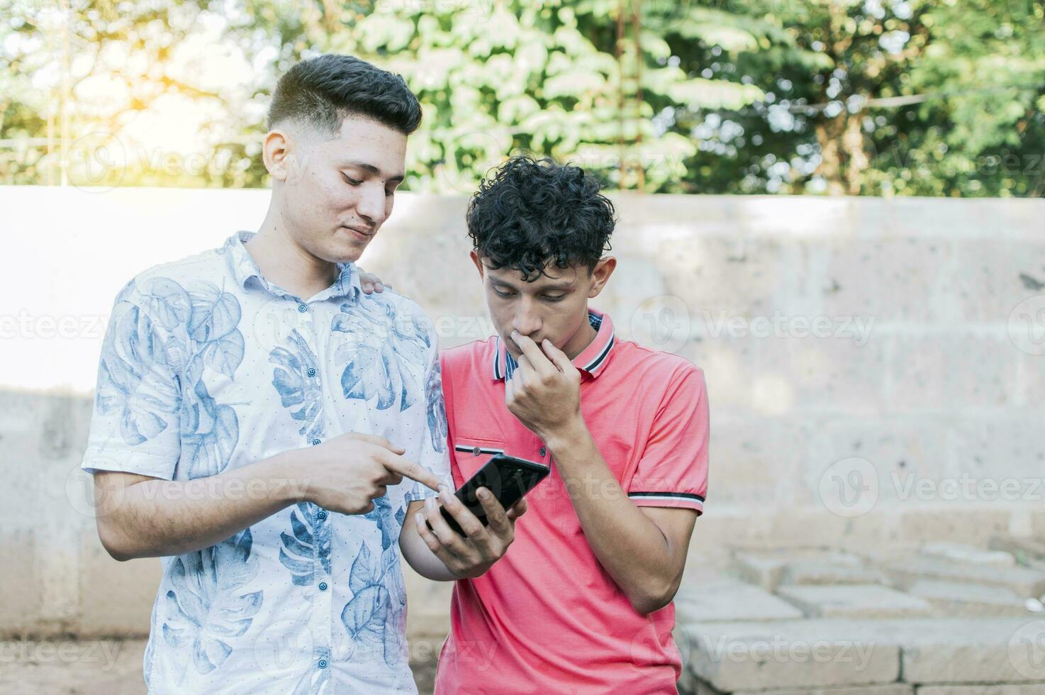 A guy showing his cell phone to another guy, Teenager explaining with his cell phone to another guy, A young man explaining with his cell phone to a young man photo