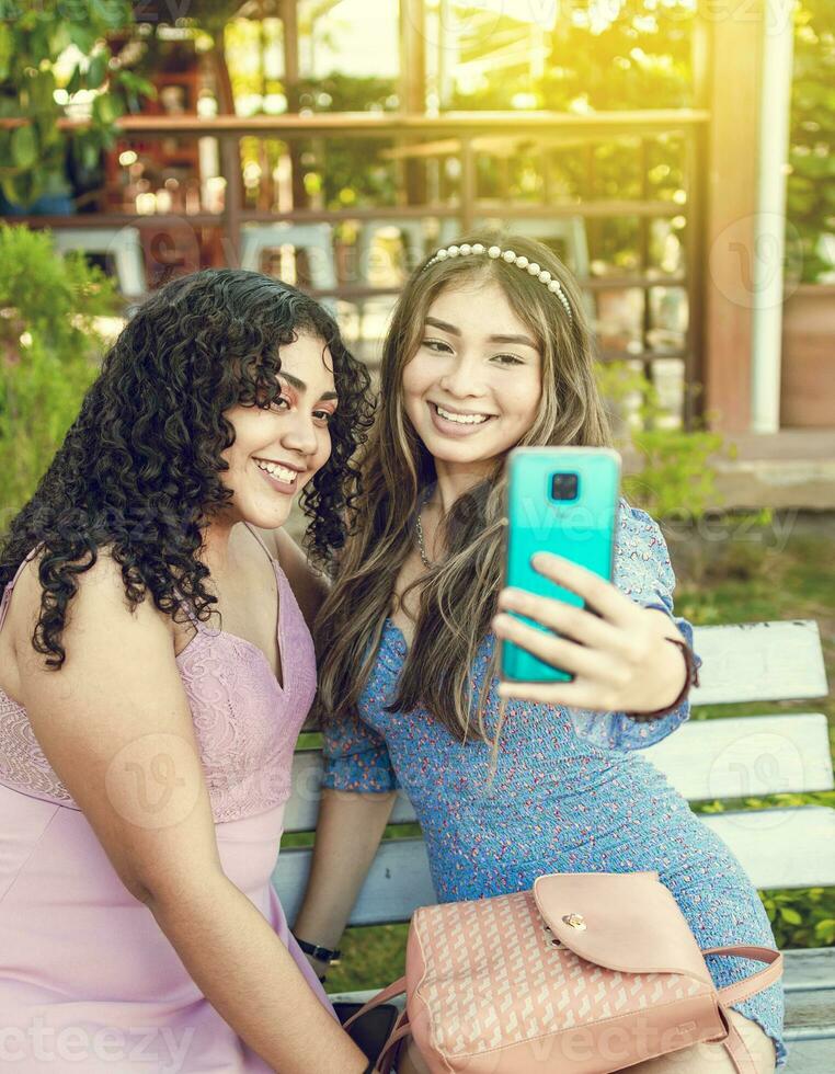 Two pretty girls sitting on a bench taking a selfie, girls smiling and taking a selfie, sisterly friendship concept photo