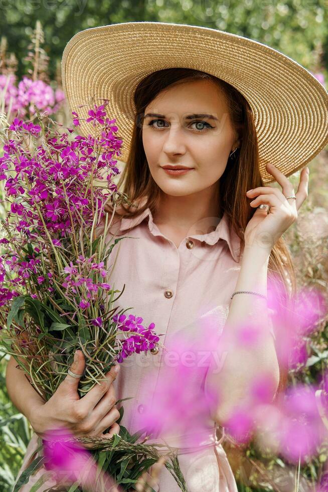 young girl in nature with a bouquet of pink wild flowers. A bouquet of Ivan-tea in the hands of a woman. photo