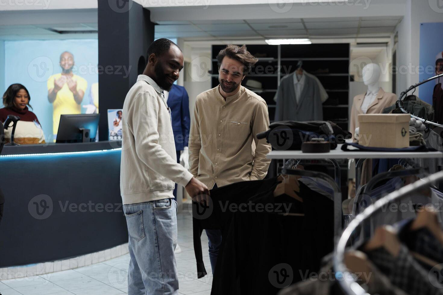 Clothing store smiling client and assistant discussing apparel style while browsing through rack. African american man showing outfit to mall customer and giving fashion advice photo