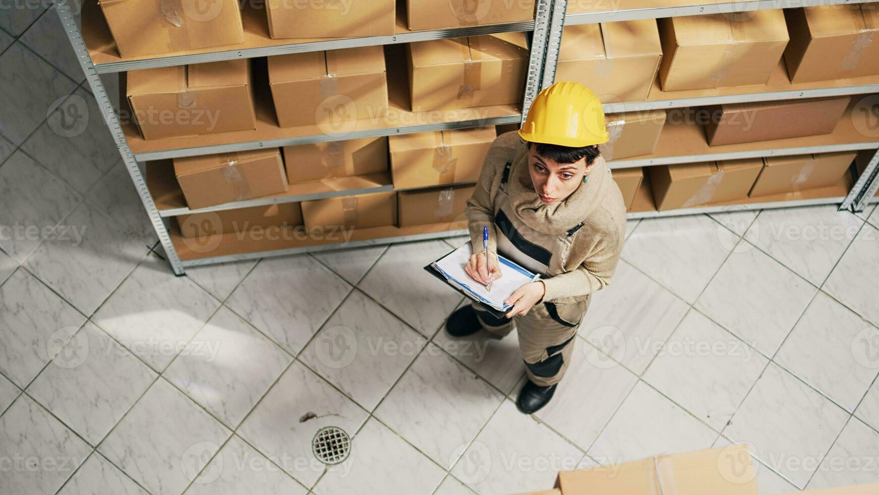 Female supervisor checking list of products on racks, looking at cardboard boxes to plan distribution. Woman with hardhat working in warehouse with merchandise and stock, storage inventory. photo