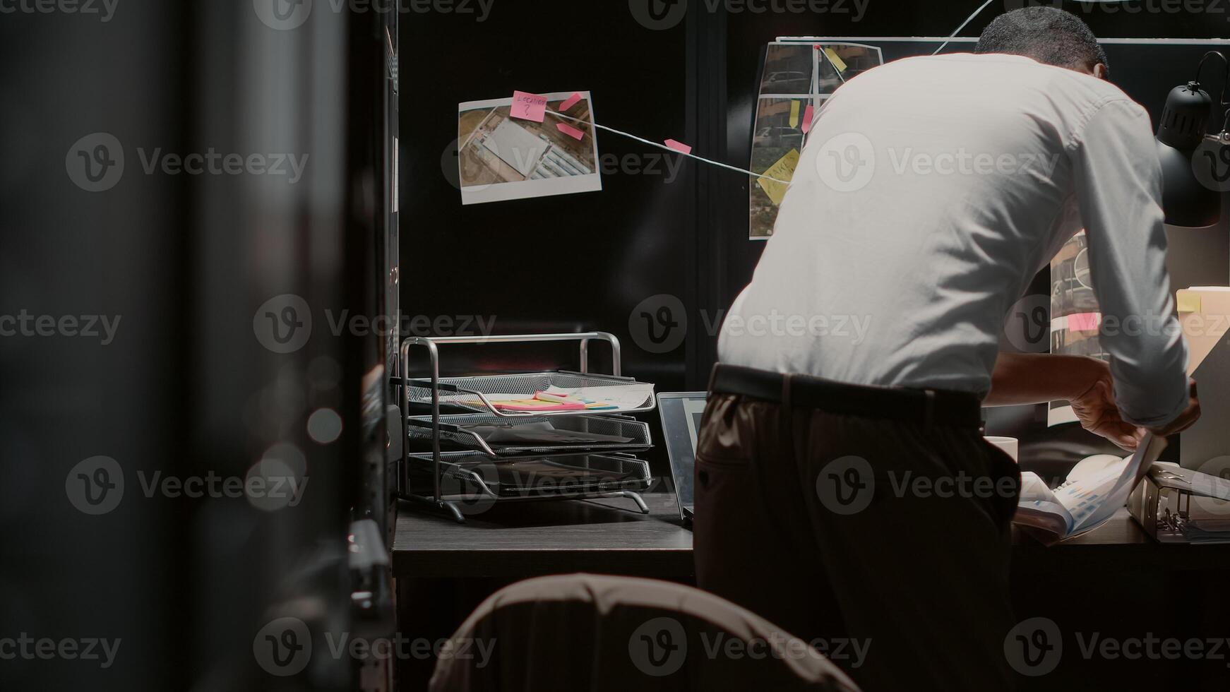 African american law agent putting clues on board, trying to conduct private investigation in incident room. Young police officer examining photos and forensic evidence on map, detective work.