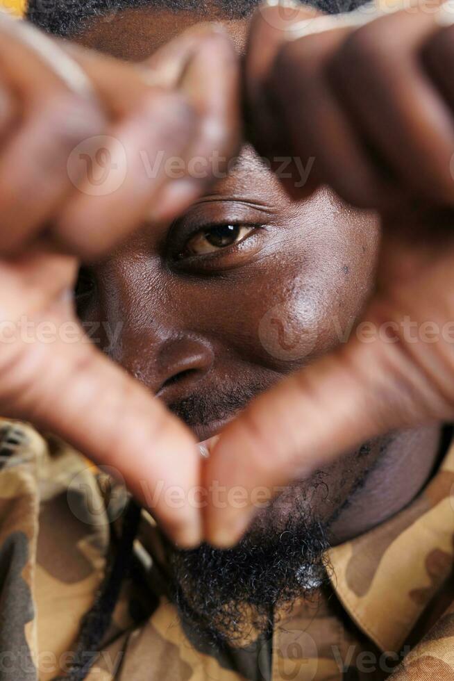 Excited man doing heart shape symbol in front of camera, smiling during valentine s day studio shot. African american person making love sign with fingers over yellow background. Positive concept photo