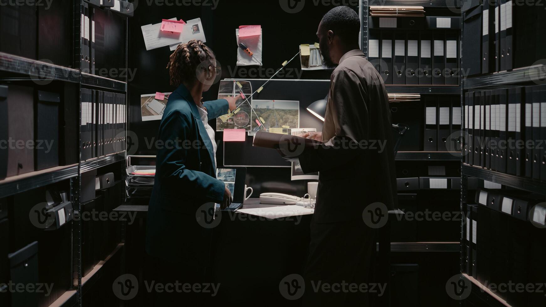 African american officers talking about evidence in office, looking at case files to find suspect. Team of investigators reading statements in police archive space, doing background checks. photo