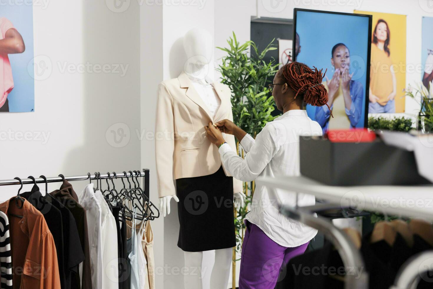 Clothing store woman assistant adjusting formal female outfit on mannequin. Fashion apparel showroom employee dressing dummy model in office wear to showcase customers new arrival photo