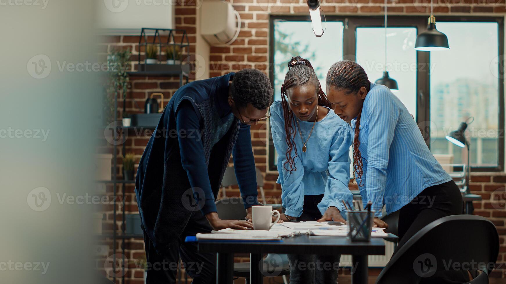Women colleagues reading analytics files on office desk, reviewing official annual data reports on documents for business development. Team of people meeting in boardroom coworking space. photo