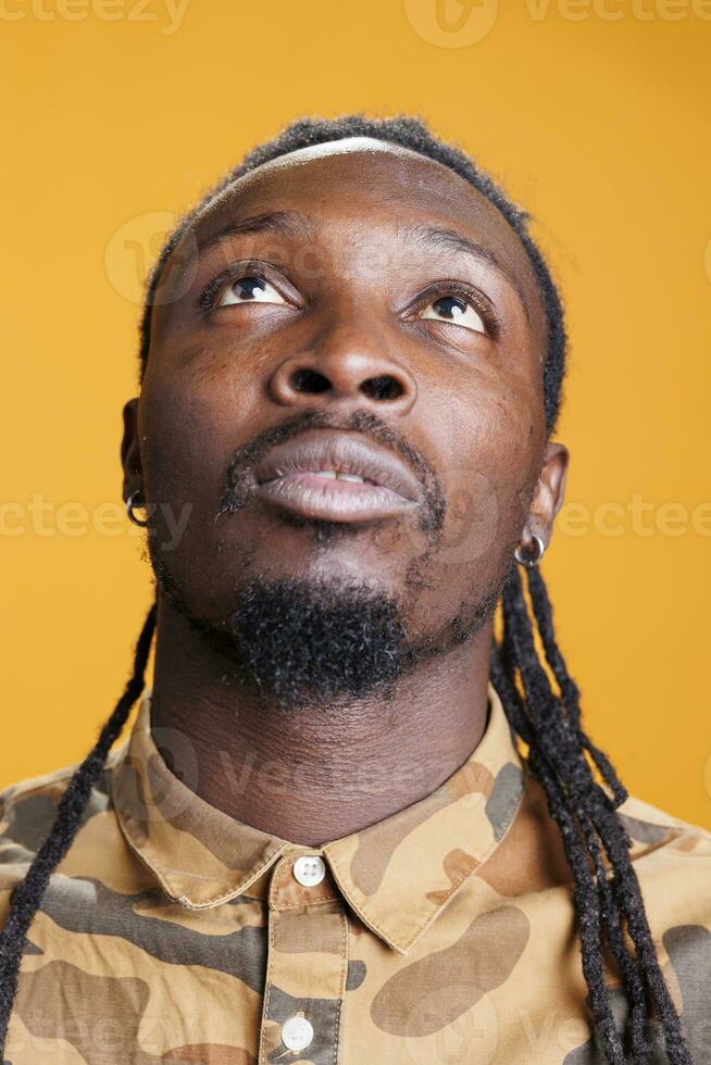 Hopeful man begging for good luck and fortune, asking god for forgiveness. Religious african american person doing prayer hands in front of studio camera over yellow background. Spirituality concept photo