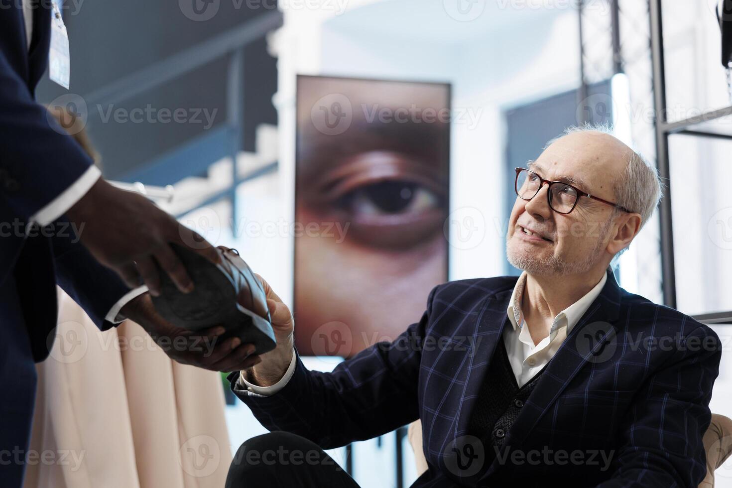 Showroom employee helping senior client with fashionable shoes in shopping centre. Elderly man buying merchandise clothes, analyzing fashion collection in boutique. Fashion concept photo
