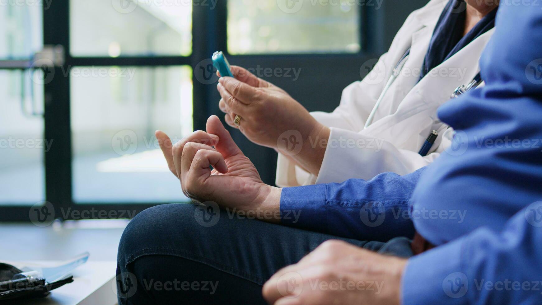 Old patient doing diabetes rutine control with glucometer instrument, specialist measuring glucose sugar level at insulin test. Doctor checking blood sample for diabetic senior man in hospital area. photo