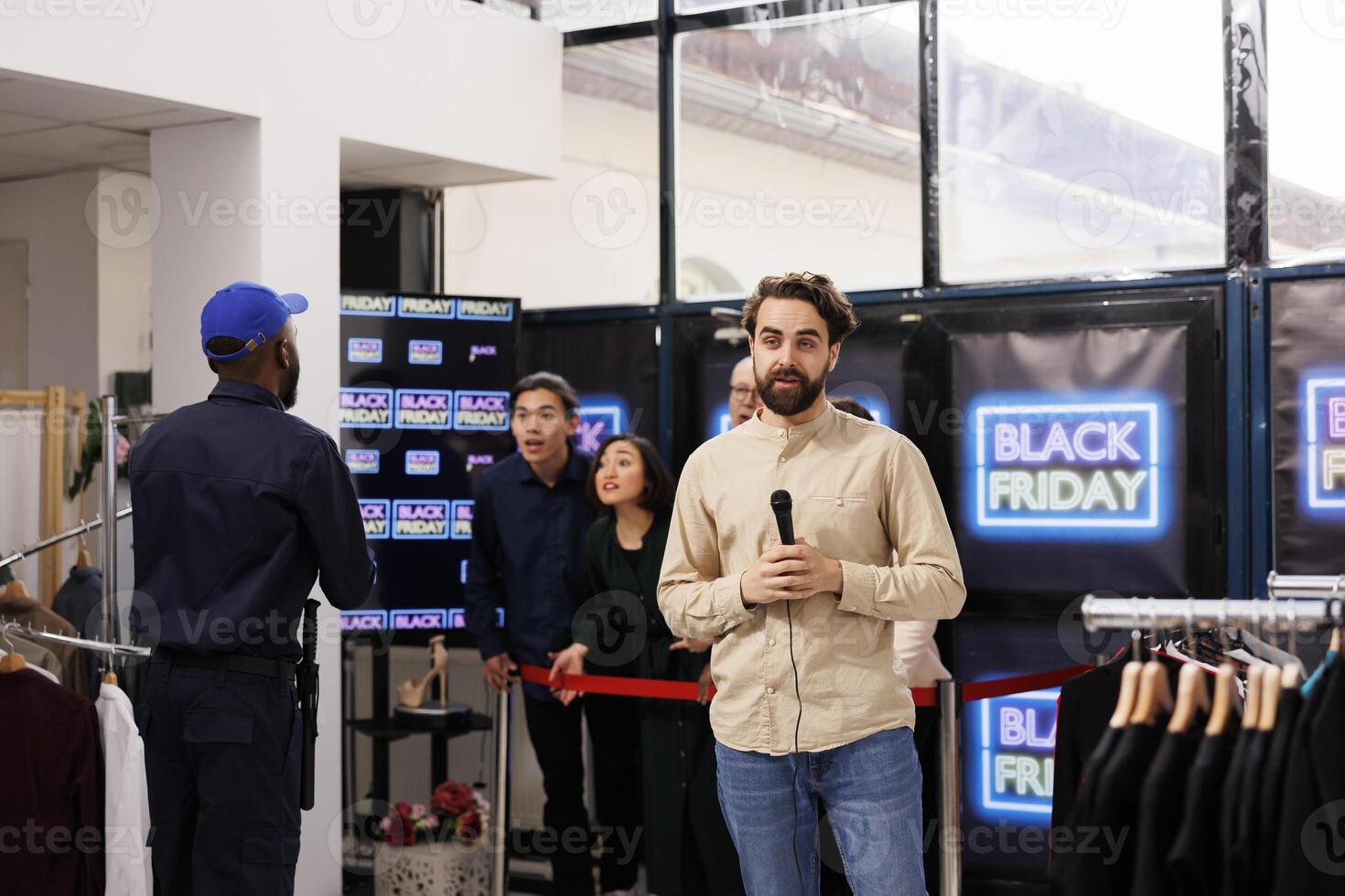Young man TV reporter covering news realtime, live streaming during Black Friday sales. Correspondent standing at store entrance talking into microphone making live newscast about shopping madness photo